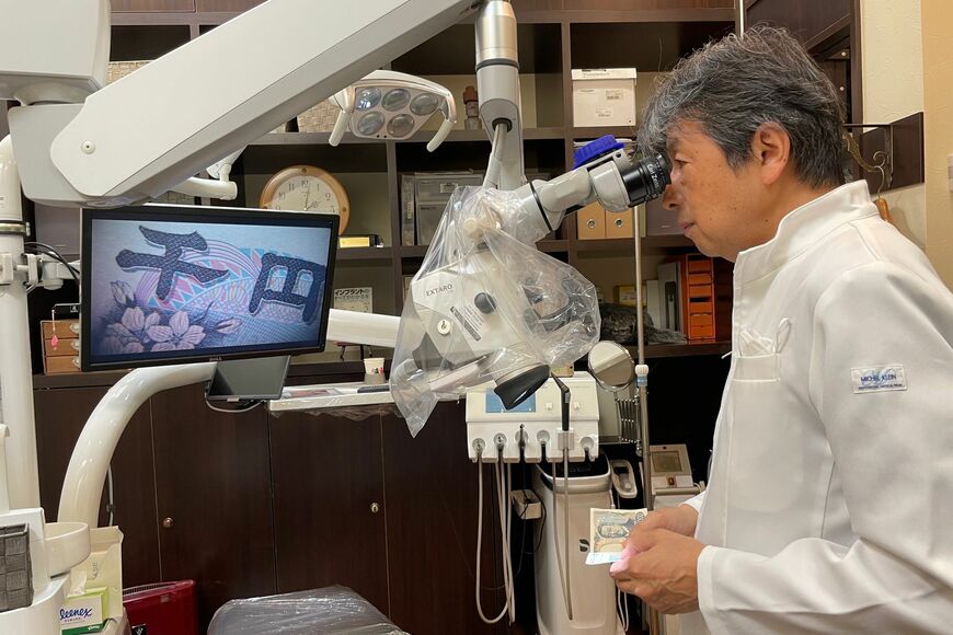 吉田さんのところでは顕微鏡を使って歯科治療を行っている。写真は1000円札を使って顕微鏡について説明する吉田さん（写真：吉田さん提供）