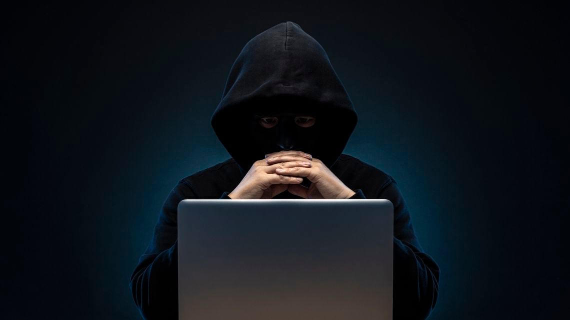 フードを被り顔を隠した男とノートパソコン