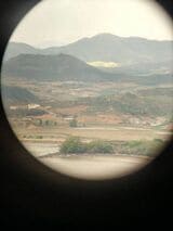 双眼鏡から見えた北朝鮮の景色。水辺のあたりに複数の人影が映っている（著者撮影）