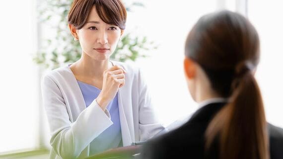 向かい合わせに座っているスーツを着た女性と会話するミドルの女性