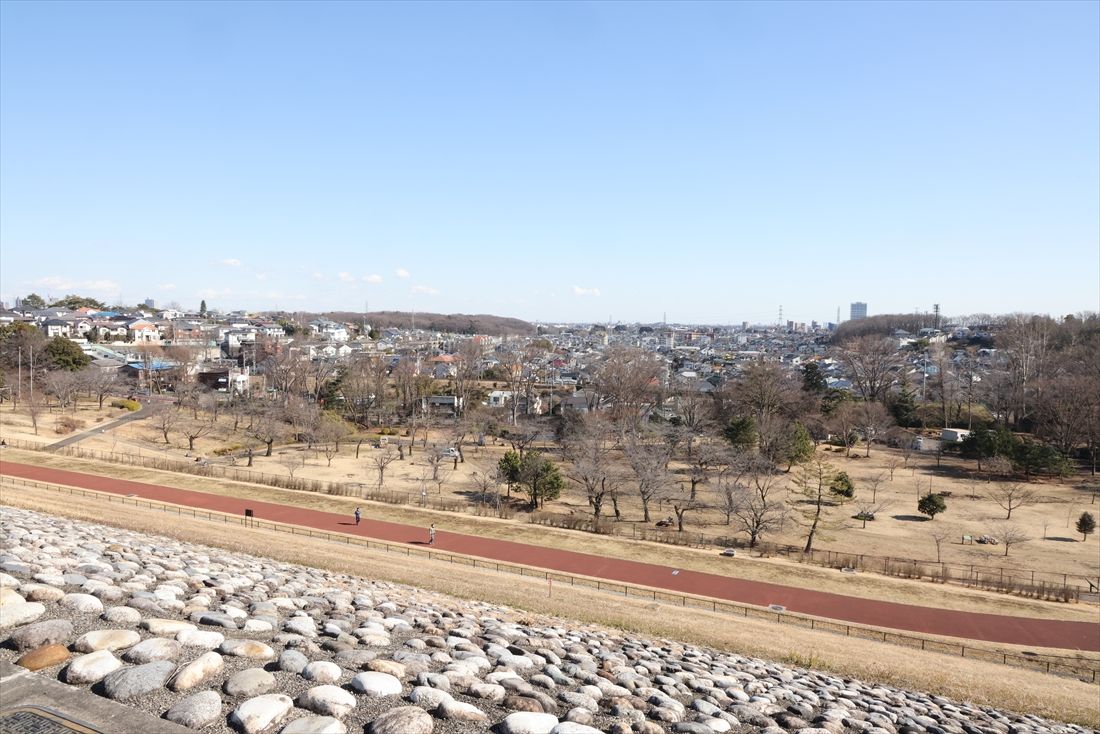 村山貯水池から狭山公園を望む。公園の右上に見える築堤が初代村山貯水池駅→狭山公園前駅→多摩湖駅跡で、左に見える跨線橋が現在の西武遊園地駅。その間にある鉄橋の向こう側が村山貯水池前駅→狭山公園駅→二代目村山貯水池駅。なお、（旧）西武鉄道は右手前に300m延伸する計画があったが頓挫した（筆者撮影）