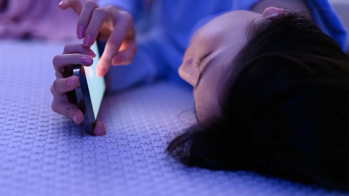 寝転んでスマホをいじる10代女性