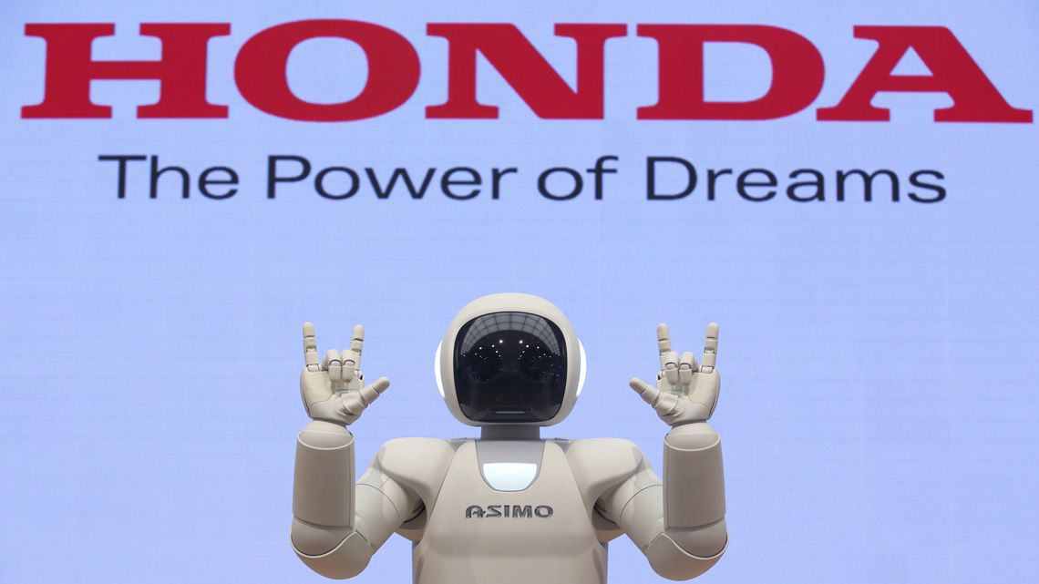 ホンダのロゴを背景にポーズをとるアシモ