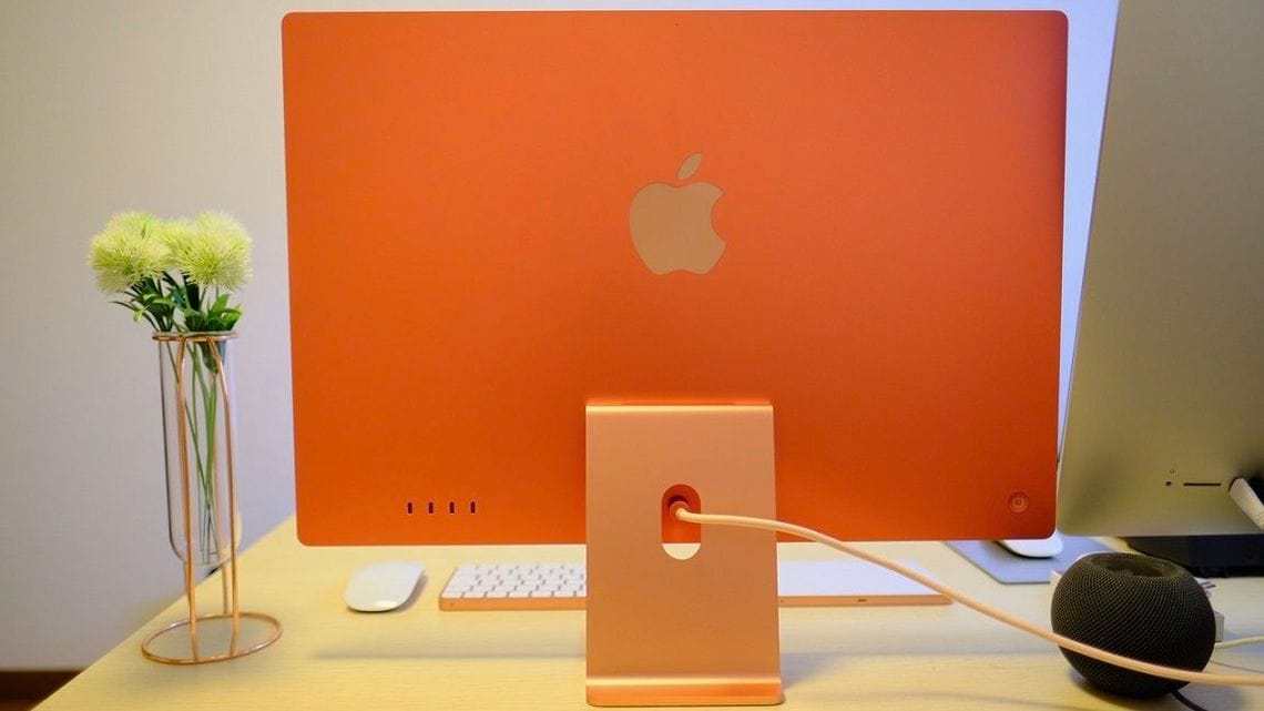 iMac（M1）オレンジ。鮮やかに染め上げられた背面は、新しいiMacのデザインを象徴する。ポートはThunderbolt 2ポート、USB-C 2ポート。中央には独自規格の磁石で接続する電源ケーブルが伸びており、上位モデルの電源アダプターにはEthernetポートも備える（筆者撮影）