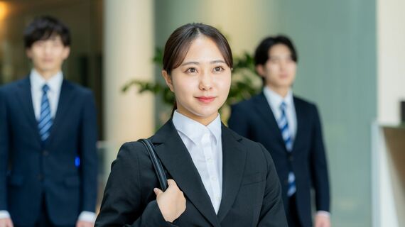 リクルートスーツ姿の女性、その後ろにスーツの男性2人