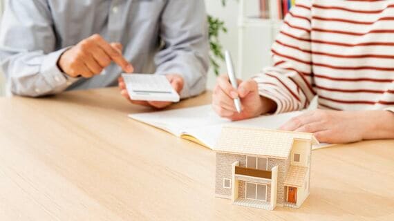 家計を計算する夫婦と家の模型