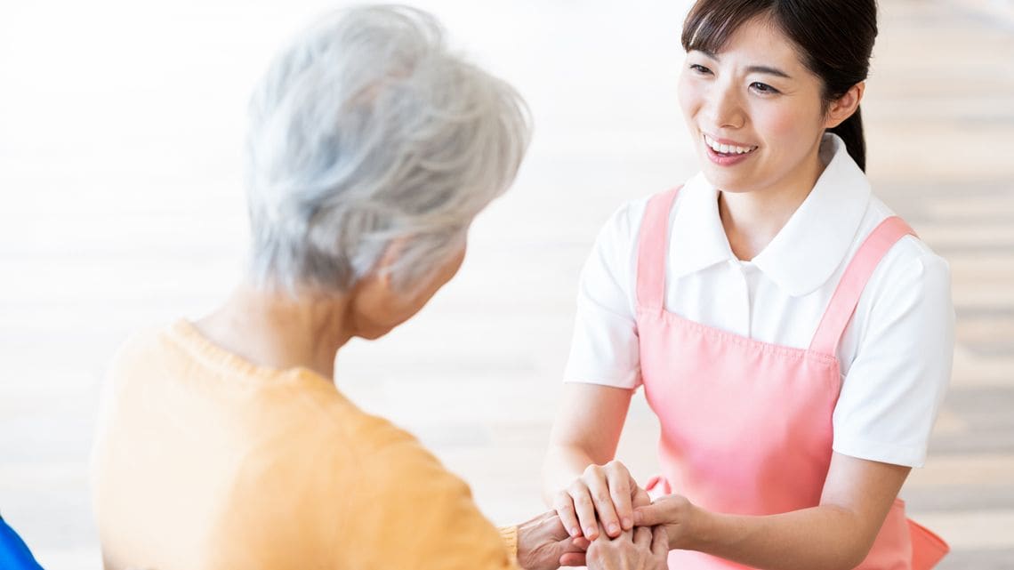 介護のイメージ写真。高齢女性の手を握る笑顔の介護士