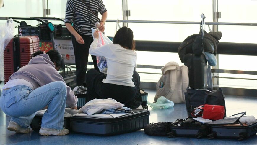 空港の出発ロビーでスーツケースの荷物を詰め替える外国人観光客