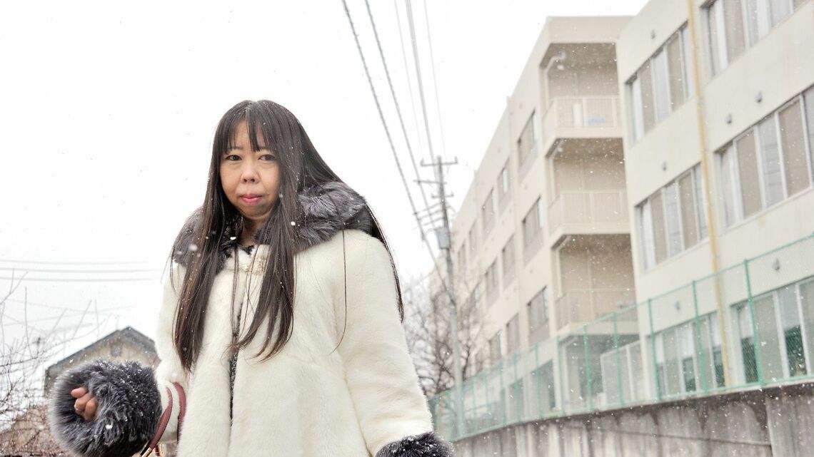 4年間入院していた多摩病院の前に立つ米田恵子さん。奥の建物の4階の閉鎖病棟でほとんどの時を過ごした。この日のように雪の日もあったが、窓から眺めることしかできなかったという（撮影：梅谷 秀司）