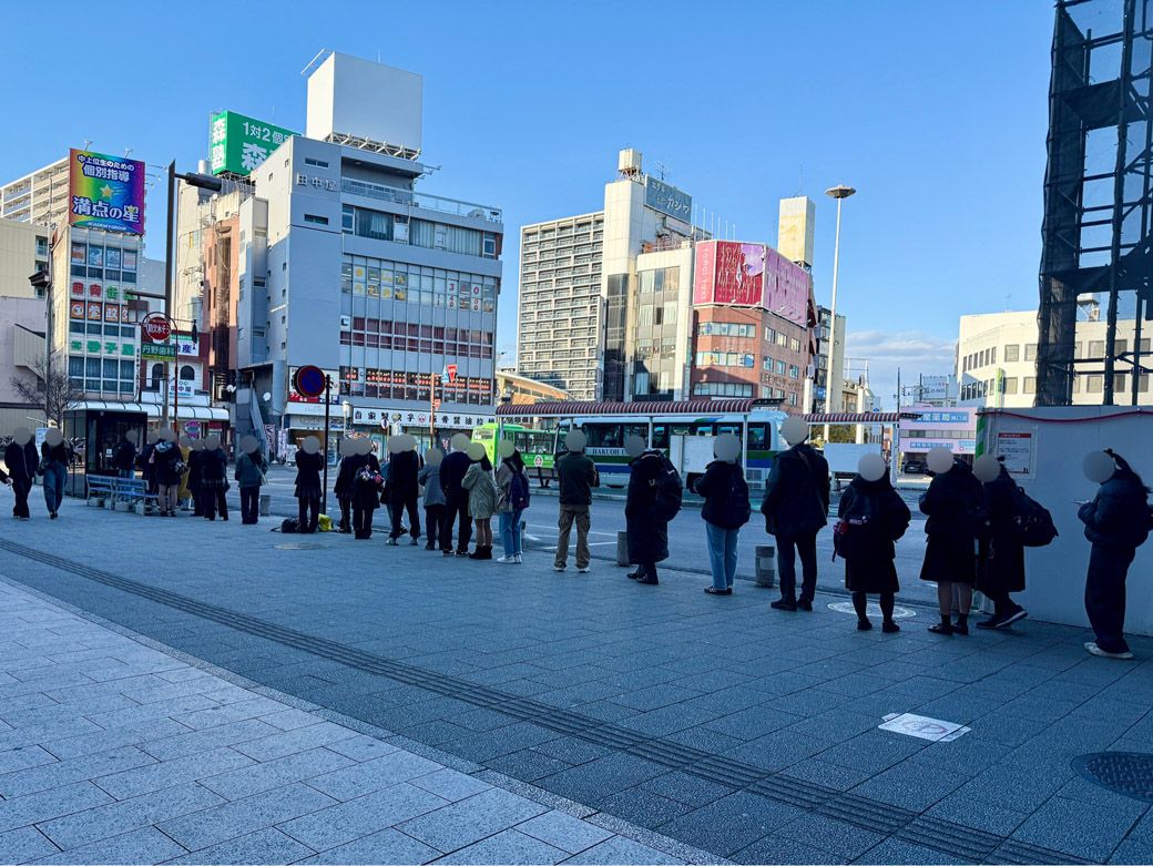 小山駅前のバス停に並ぶ人々