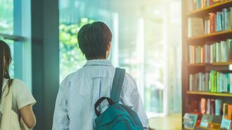 本棚が並ぶ図書館を歩く学生