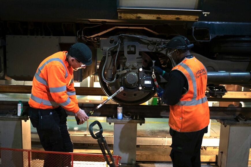イギリスの鉄道の現場で、センサーを台車に取り付ける作業員（写真：日立製作所）