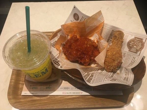 bb.qオリーブチキンカフェの定番、オリーブチキン（右290円）とヤンニョムチキン（左350円）。ドリンクは、ダブルレモン製法で仕上げられた生搾りレモネード（290円）。オリーブチキンは食感といい味わいといい軽さが特徴で、1本では物足りないと感じるほど。ヤンニョムチキンは韓国ドラマ「愛の不時着」により、日本での人気が高まった（筆者撮影）