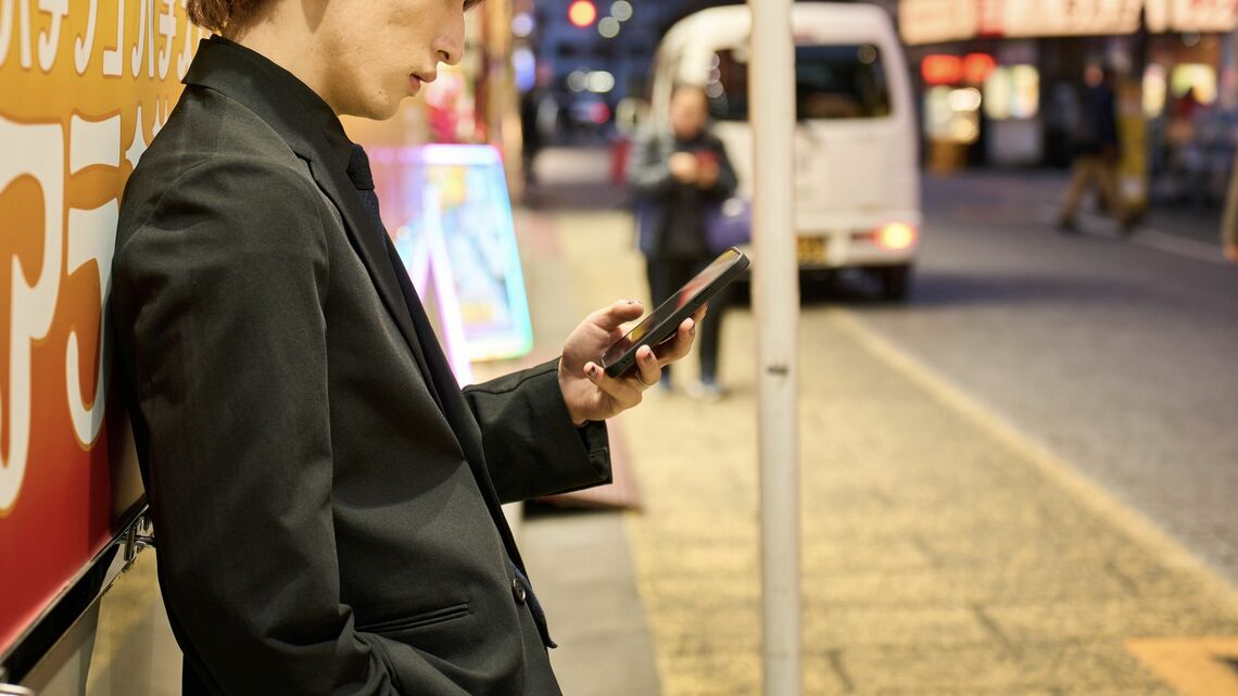 壁に寄りかかっってスマホを触るホスト