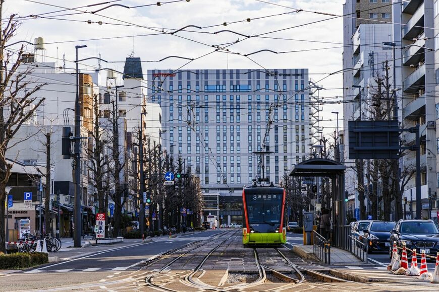 松山城のお堀端を目指して走る伊予鉄市内電車。バックに見えるのは松山市駅のターミナルビル（撮影：鼠入昌史）
