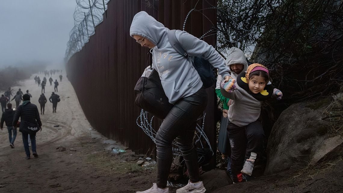 アメリカとメキシコの国境フェンスの隙間を通過する女性と子ども