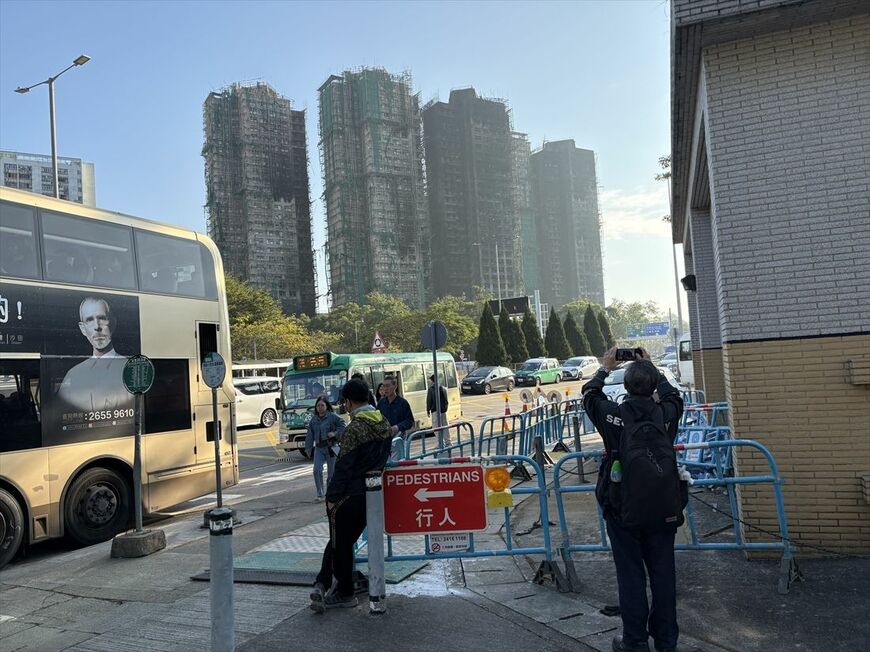バス停から火災の現場方向を撮影する通行人と、通常運行を続ける道路（筆者撮影）
