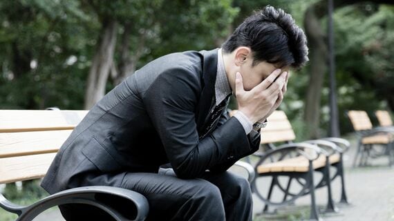 ベンチに座り頭を抱えて落ち込むスーツ姿の男性