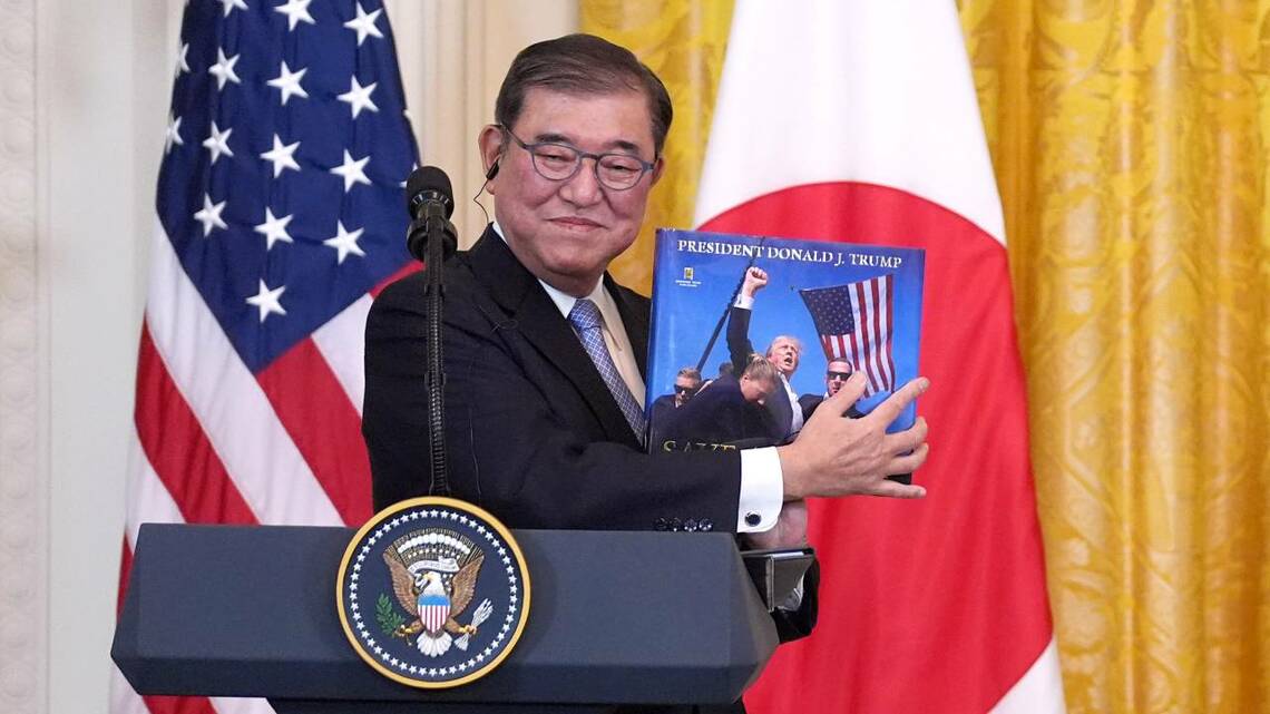 日米首脳共同会見でトランプ大統領の写真を掲げる石破首相。「会談成功」との評価が広がっているが、それは重大な視点が欠けている（写真：AP／アフロ）