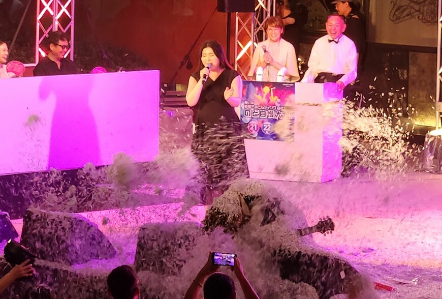 シュレッダーの紙吹雪に埋もれるTK（写真前）の後ろで「I'm proud」を歌い上げる様子に、司会者と審査員だけでなく会場が爆笑した（記者撮影）