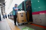 車内から台車に載せられた荷物を運び出す（記者撮影）