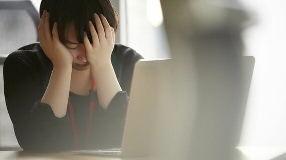 手で顔をおおう女性 紺色の服 パソコン