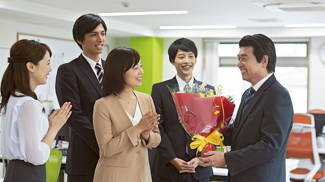 花束を手に、笑顔と拍手で見送られる定年退職者