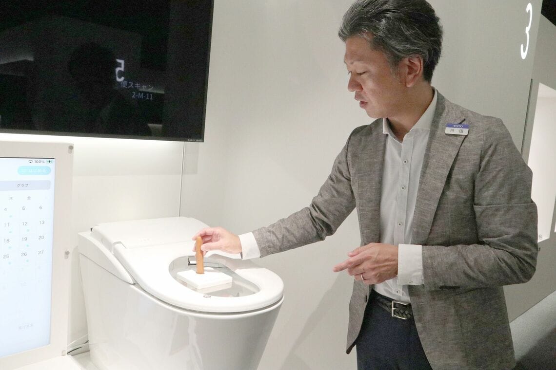 テスト機に模擬便を投入する川田氏。落下速度も便のタイプごとに忠実に再現される（写真：筆者撮影）