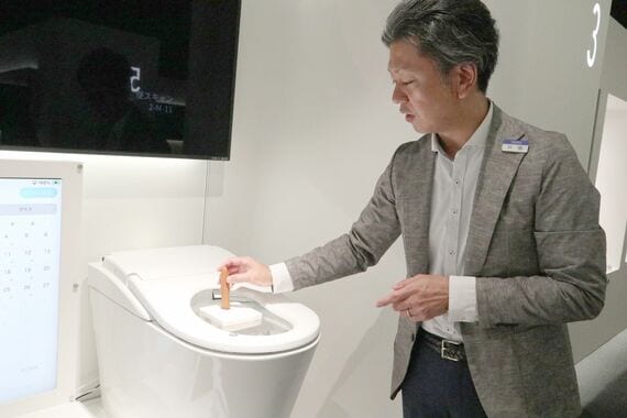 テスト機に模擬便を投入する川田氏。落下速度も便のタイプごとに忠実に再現される(写真:筆者撮影)