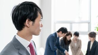 職場の仲間を離れたところで見つめる男性