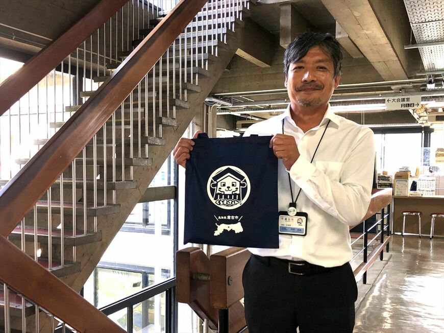 「倉吉市周遊滞在型観光地モビリティ向上計画」の策定に携わる、倉吉市総務部企画課・課長補佐兼企画係長の鳥飼真輔氏。倉吉市役所にて「くらすけくん」グッズを持って（筆者撮影）