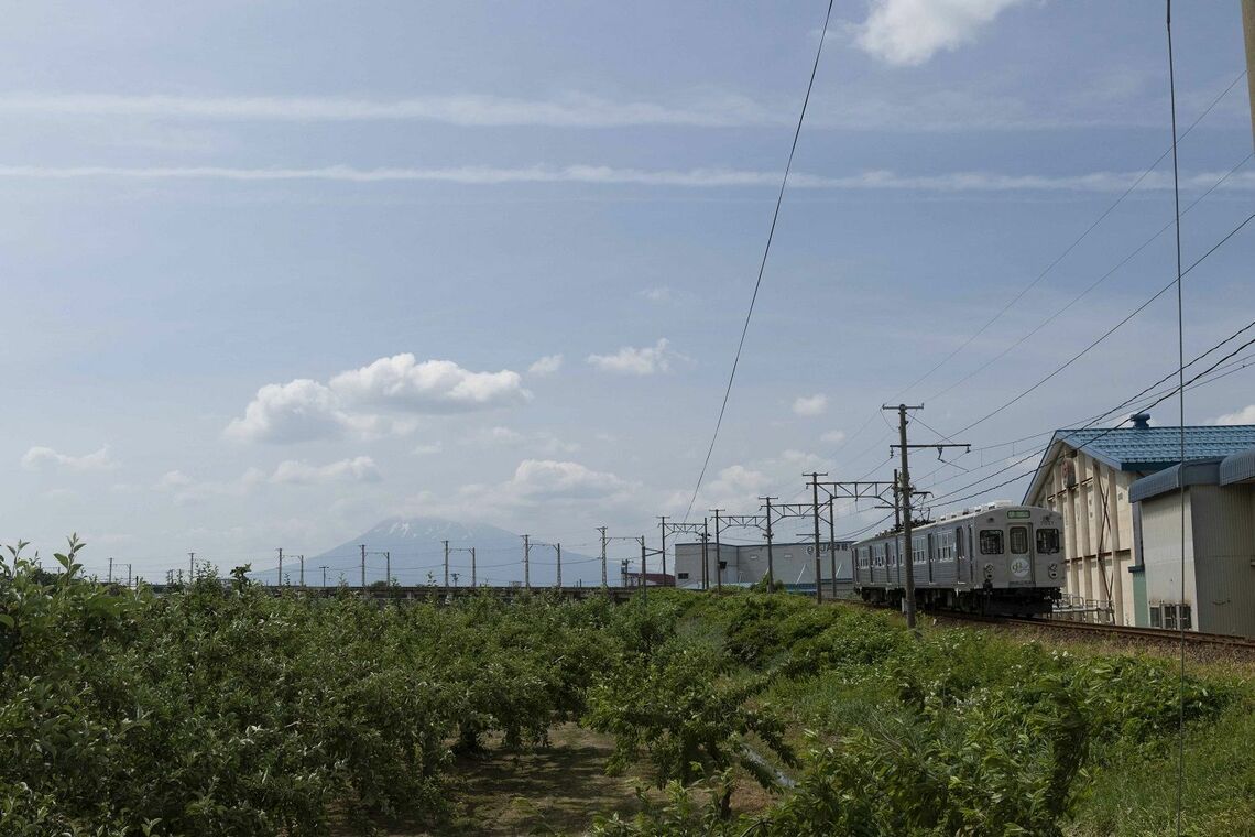 津軽といえばリンゴ。畑の横をゆく弘南鉄道大鰐線（撮影：鼠入昌史）
