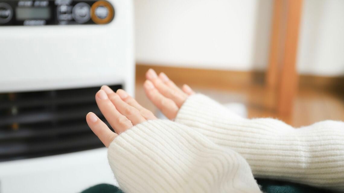 ファンヒーターで暖まる女性