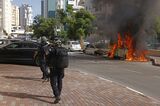 イスラエルで、ロケット弾攻撃を受けて炎上する車を通過する治安部隊（写真： Bloomberg）