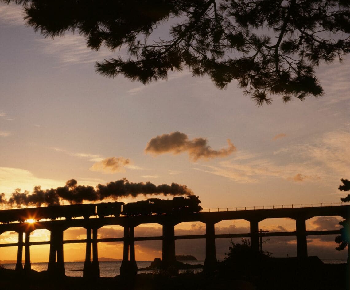 夕陽に照らされた山陰本線のコンクリート橋を行くD51形牽引の列車（撮影：南正時）