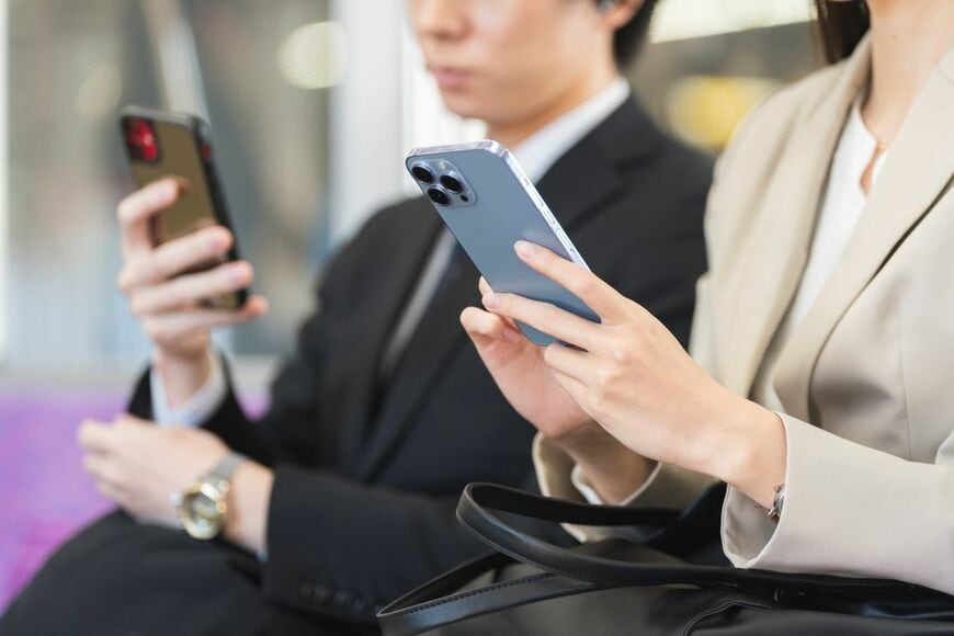 電車の中でスマートフォンを操作するビジネスパーソン