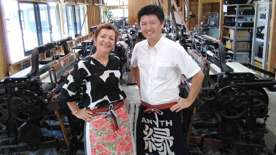 自社工場の織機と前掛けをした西村社長と女性