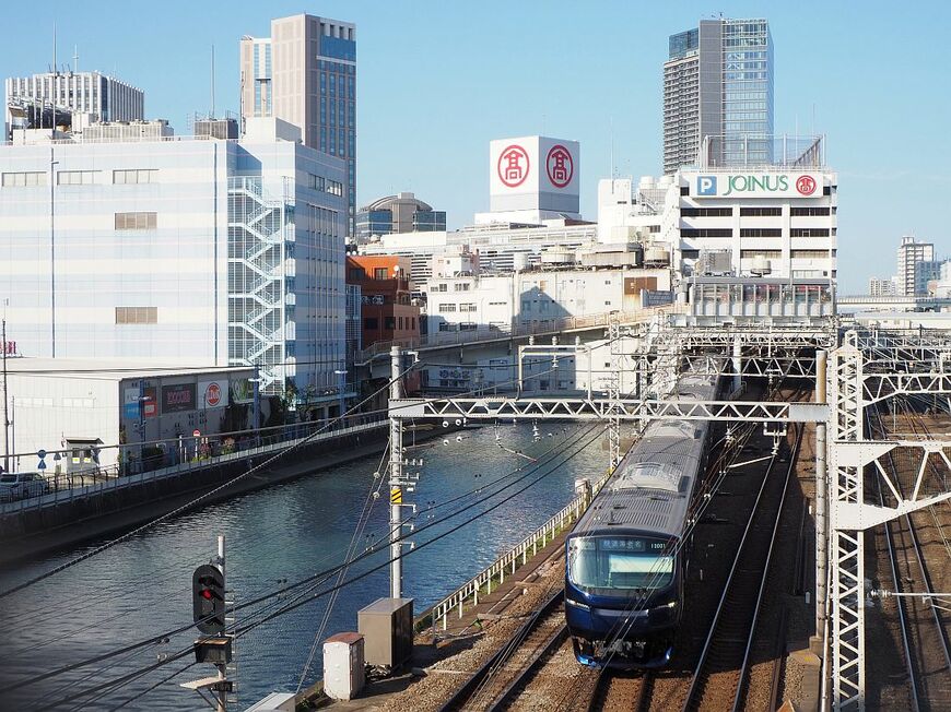 平沼橋から見た横浜駅西口付近。高島屋と相鉄ジョイナス、そして左側の帷子川沿いに相鉄ムービルが見える。相鉄線の電車は最新の13000系（編集部撮影）