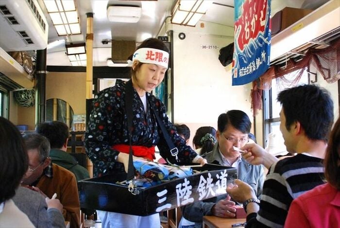 車内で「うに弁当」を売る海女の衣装を纏った売り子