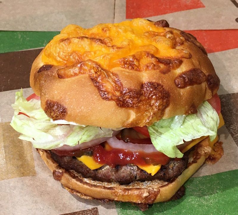 チーズアグリービーフバーガー（740円）。バンズは4種類のチーズを採用し、発酵前、焼成前の2段階でトッピングすることで、チーズの味と香りをより高めた。香ばしく、野性味があるビーフパティとチェダーチーズ、野菜などが見た目より味重視で詰め込まれている（筆者撮影）