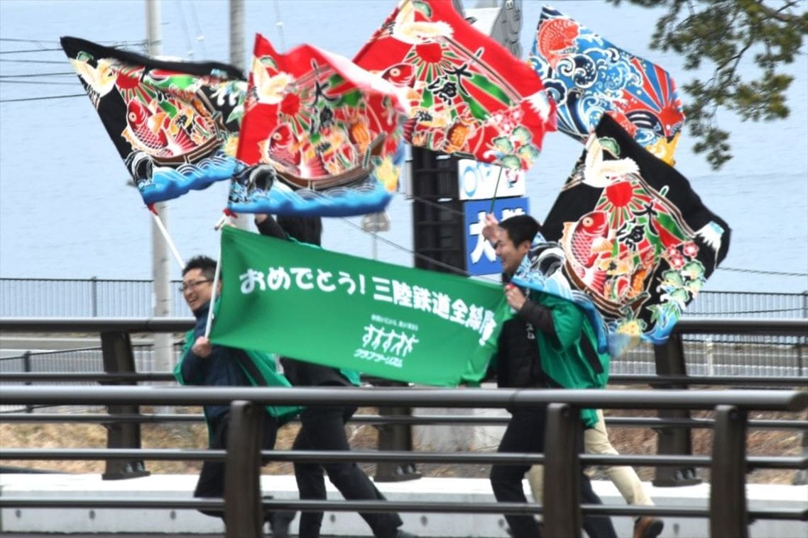 大漁旗を振って記念列車を歓迎する沿線の人々