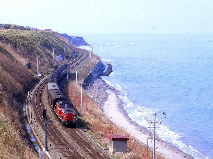 噴火湾沿いの函館本線を、旧型客車を連ねたDD51形牽引の普通列車が走る＝1977年（撮影：南正時）
