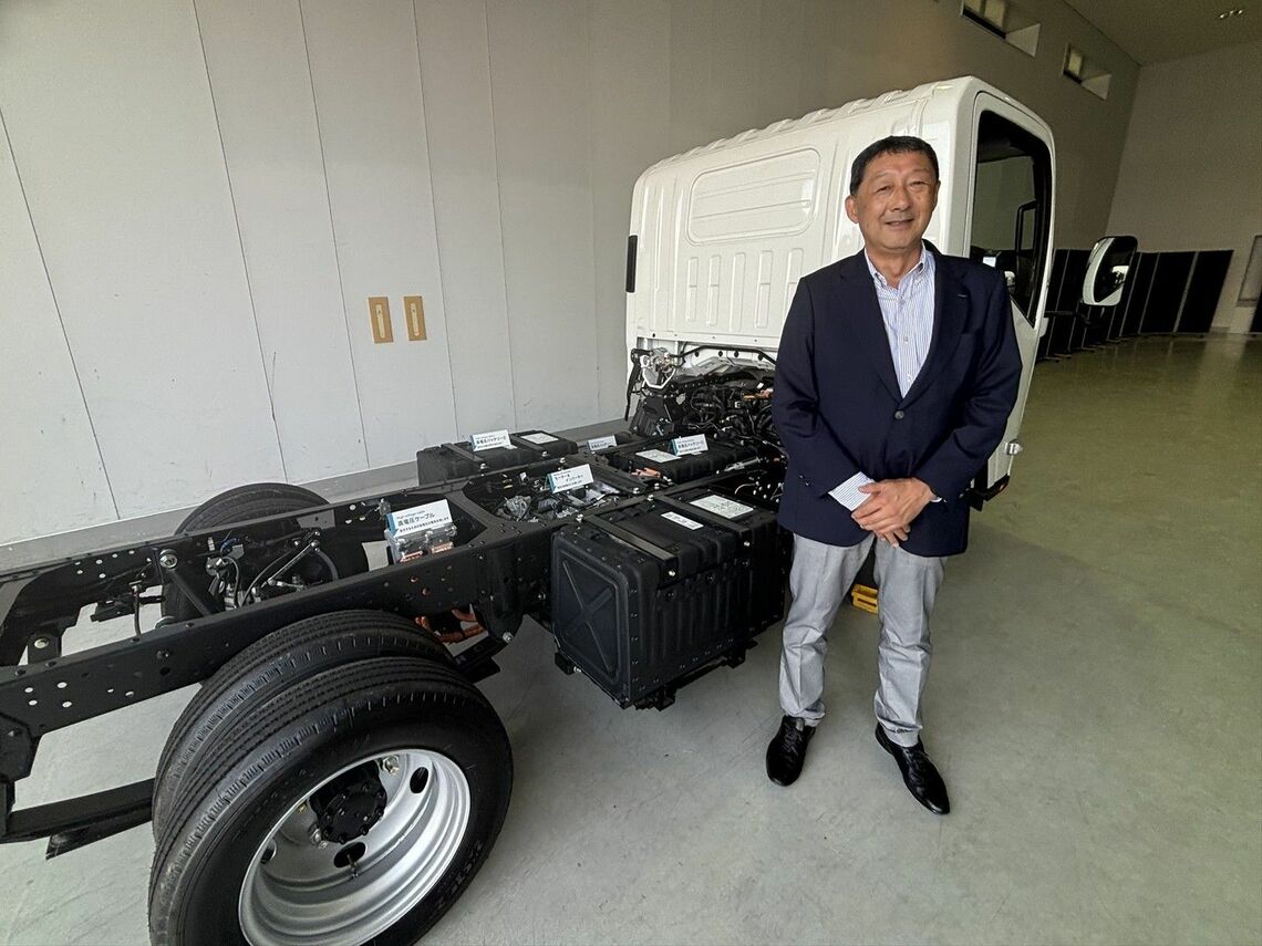いすゞの専務執行役員/カーボンニュートラル戦略部門EVPの大平隆氏。エルフ EVトラックの技術展示車両と（筆者撮影）