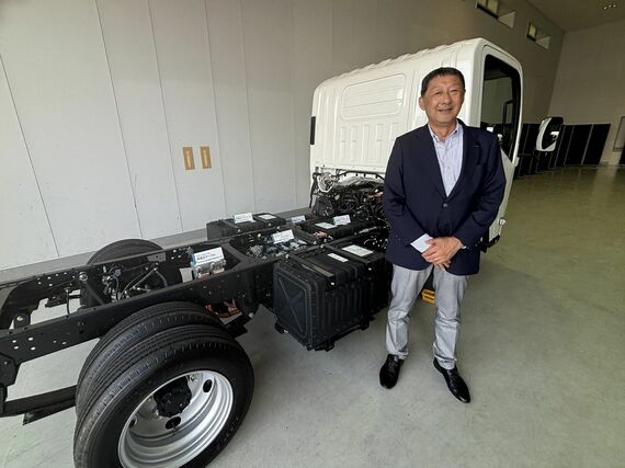 いすゞの専務執行役員/カーボンニュートラル戦略部門EVPの大平隆氏。エルフ EVトラックの技術展示車両と（筆者撮影）