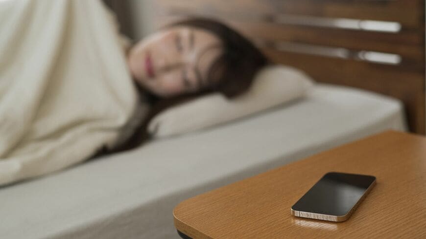 サイドテーブルにスマホを置いて寝る女性