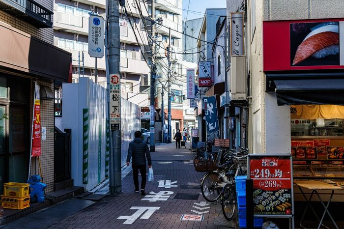 梅島駅近くの路地。工事の仮囲いの奥にマンションも見え、
