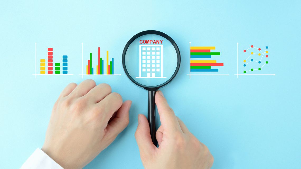グラフとビルのアイコンにルーペをあてる男性
