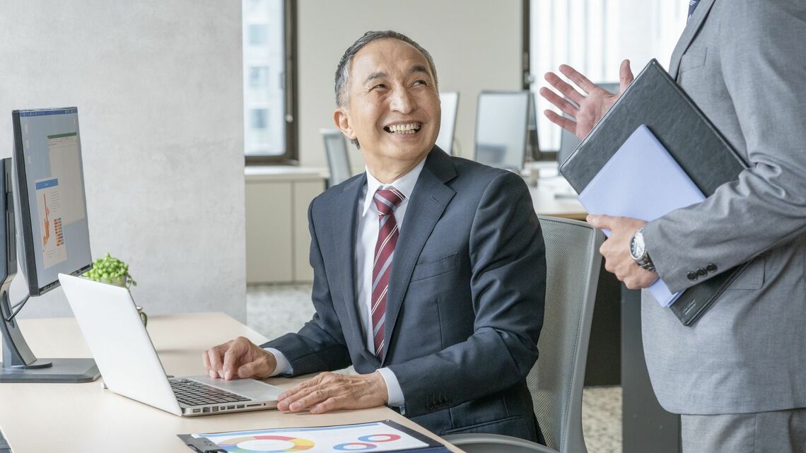 パソコン作業をしながら会話する笑顔のシニア男性