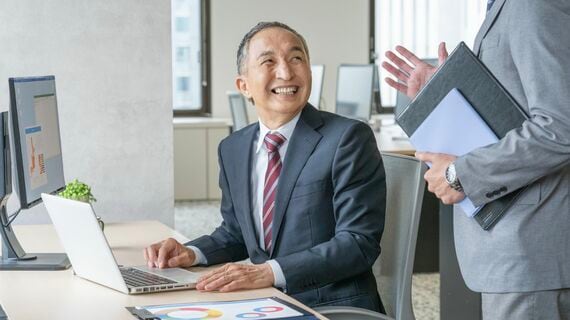 パソコン作業をしながら会話する笑顔のシニア男性