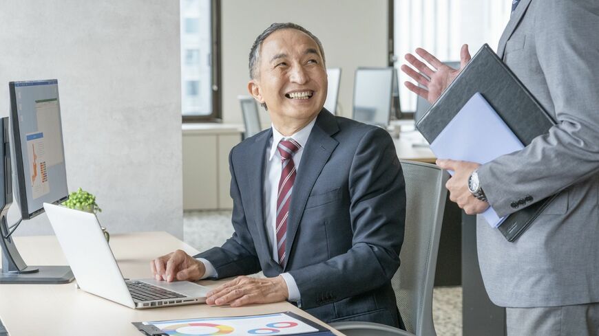 パソコン作業をしながら会話する笑顔のシニア男性